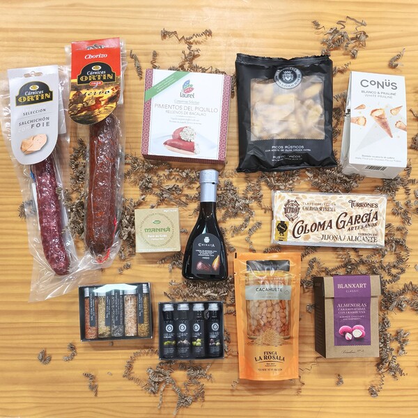 Vista aérea de una cesta gourmet de Navidad con embutidos, turron, chocolates, aceites, vinagre, sal, frutos secos, patés y pimientos de piquillo